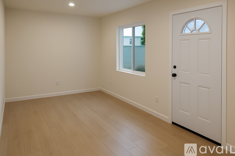 A room with a white door and a window with a view of a fence and trees.