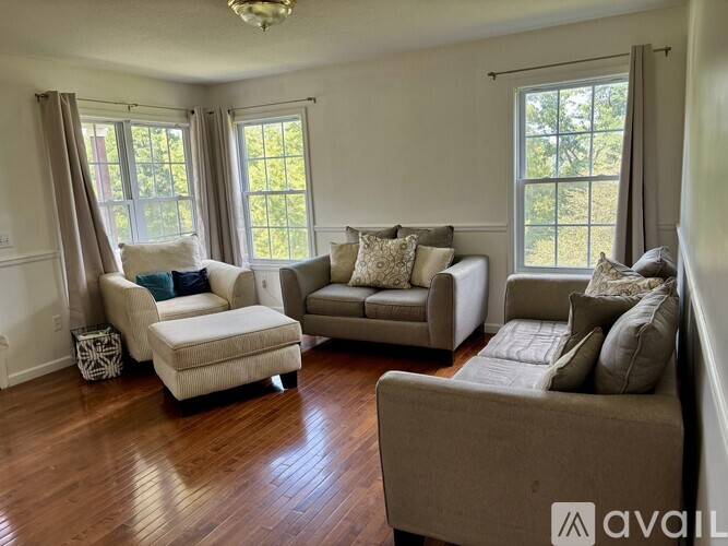 A living room with a couch, chair, ottoman, and a window.