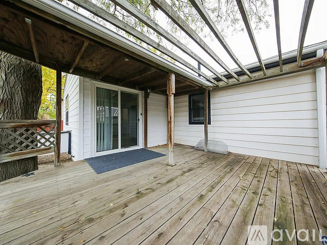 A wooden deck with a glass roof and a white house in the background.