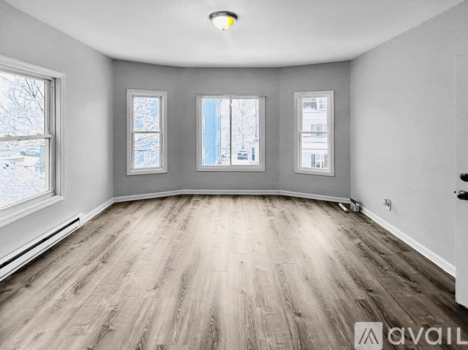 Empty room with wooden flooring and three windows.