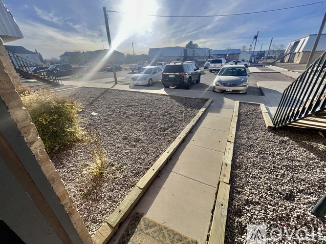 A sunny day in a parking lot with cars parked and a building in the background.
