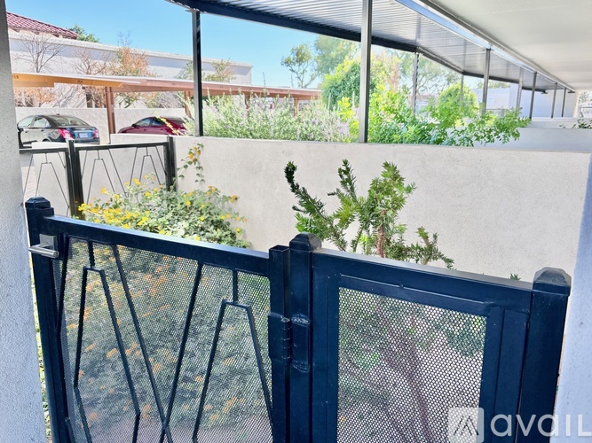 A balcony with a black railing and a view of a parking lot and trees.