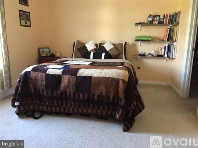A bedroom with a bed covered in a multicolored quilt and a bookshelf with various items on it.