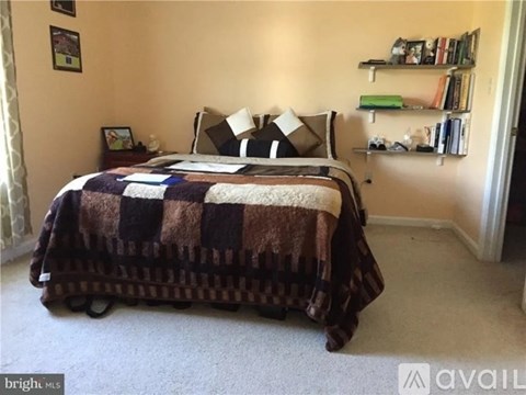 A bedroom with a bed covered in a multicolored quilt and a bookshelf with various items on it.