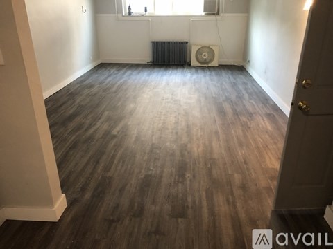 A room with wooden flooring and a window with a fan and radiator.