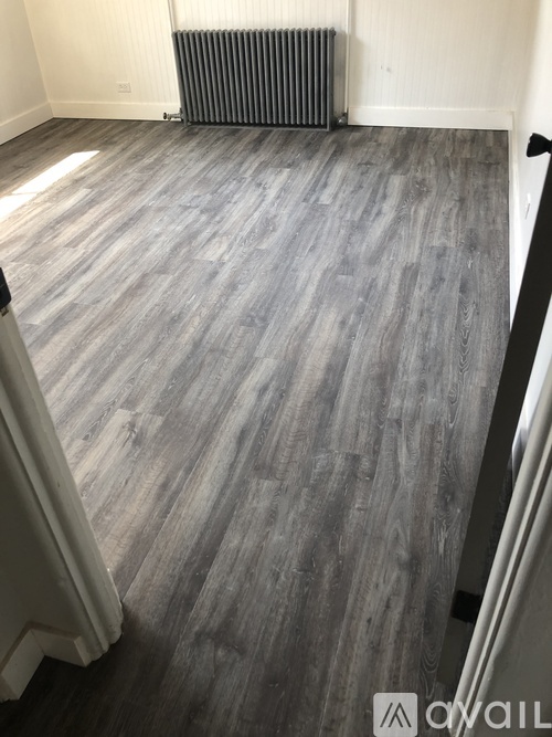 A room with a grey wooden floor and a radiator on the wall.