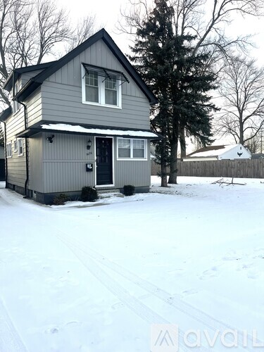 A house with a grey siding and a black door is surrounded by snow.