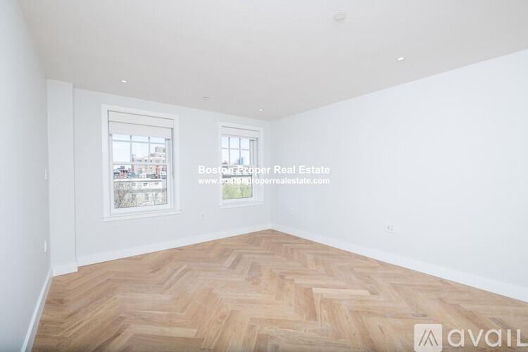 A large empty room with wooden flooring and two windows.