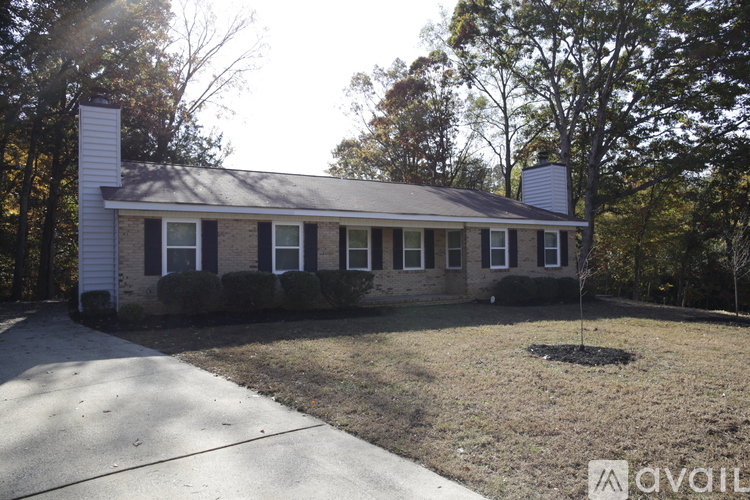 A house with a white chimney and a grey roof is surrounded by trees.
