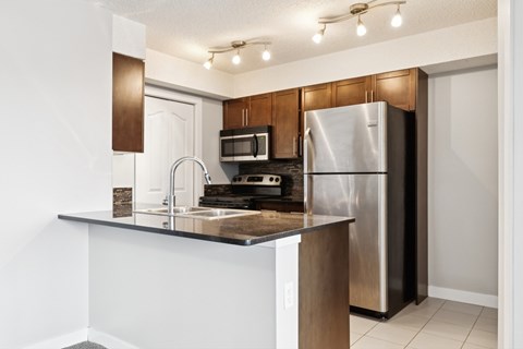 A modern kitchen with a stainless steel refrigerator and a black countertop.