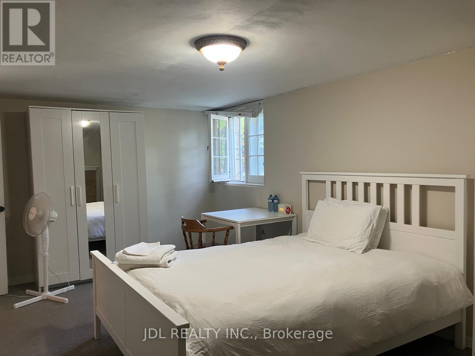 A bedroom with a bed, desk, and fan.