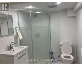 A bathroom with a toilet, sink, mirror, and shower.
