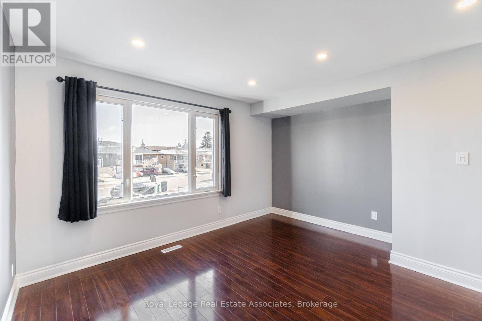 A room with wooden floors and a large window with black curtains.