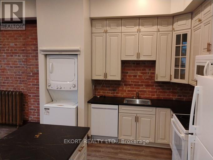 A kitchen with white appliances and a brick wall.