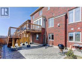 A red brick house with a wooden deck and a BBQ grill.