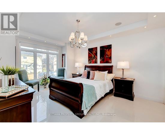 A bedroom with a large bed, a chair, and a chandelier.