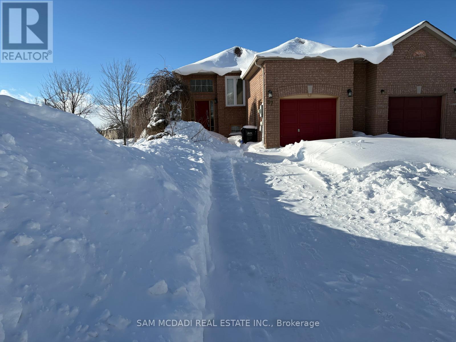 A house with a red garage door is surrounded by snow.