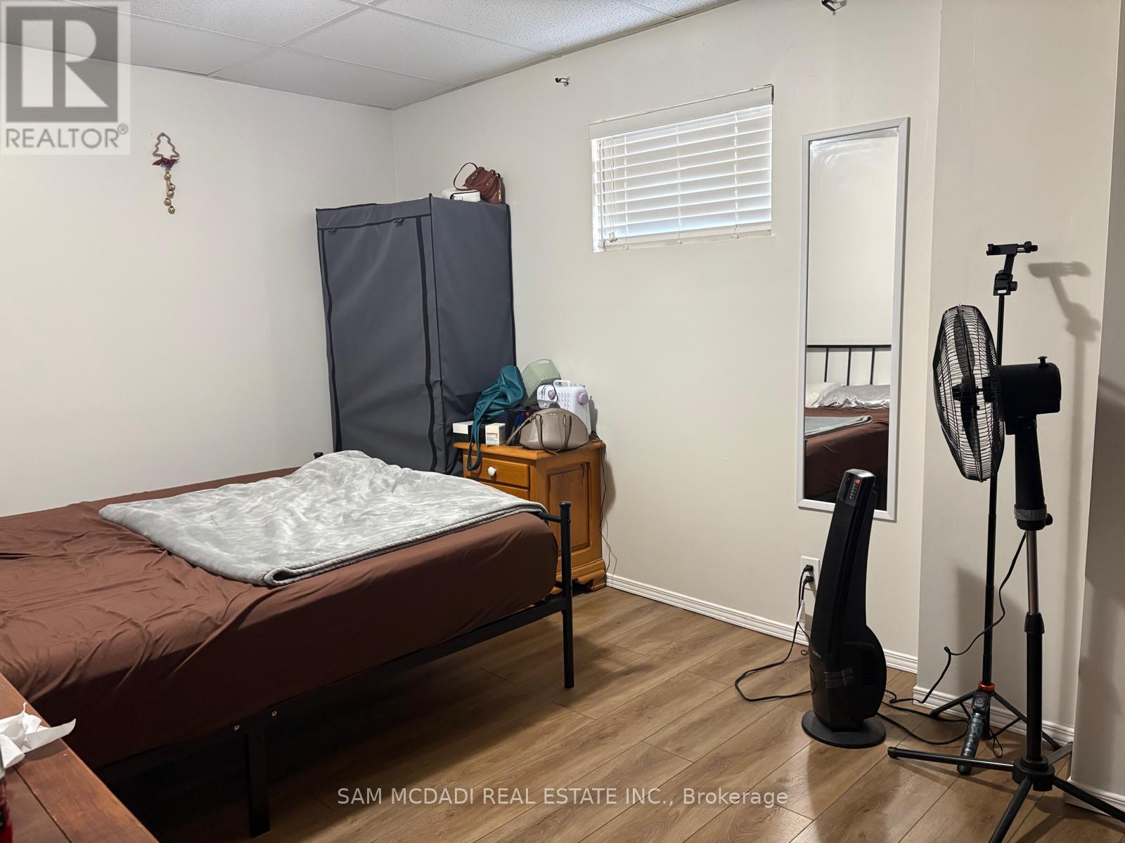 A bedroom with a bed, a wardrobe, a dresser, and a fan.