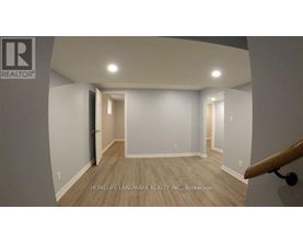 A room with a wooden floor and white walls, with a staircase on the right side.