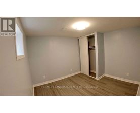 A room with a wooden floor and a white wall with a doorway leading to another room.