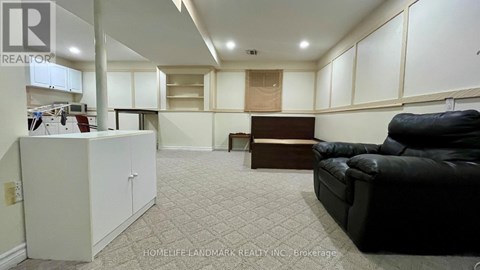 A living room with a black couch and a kitchen area with white cabinets.
