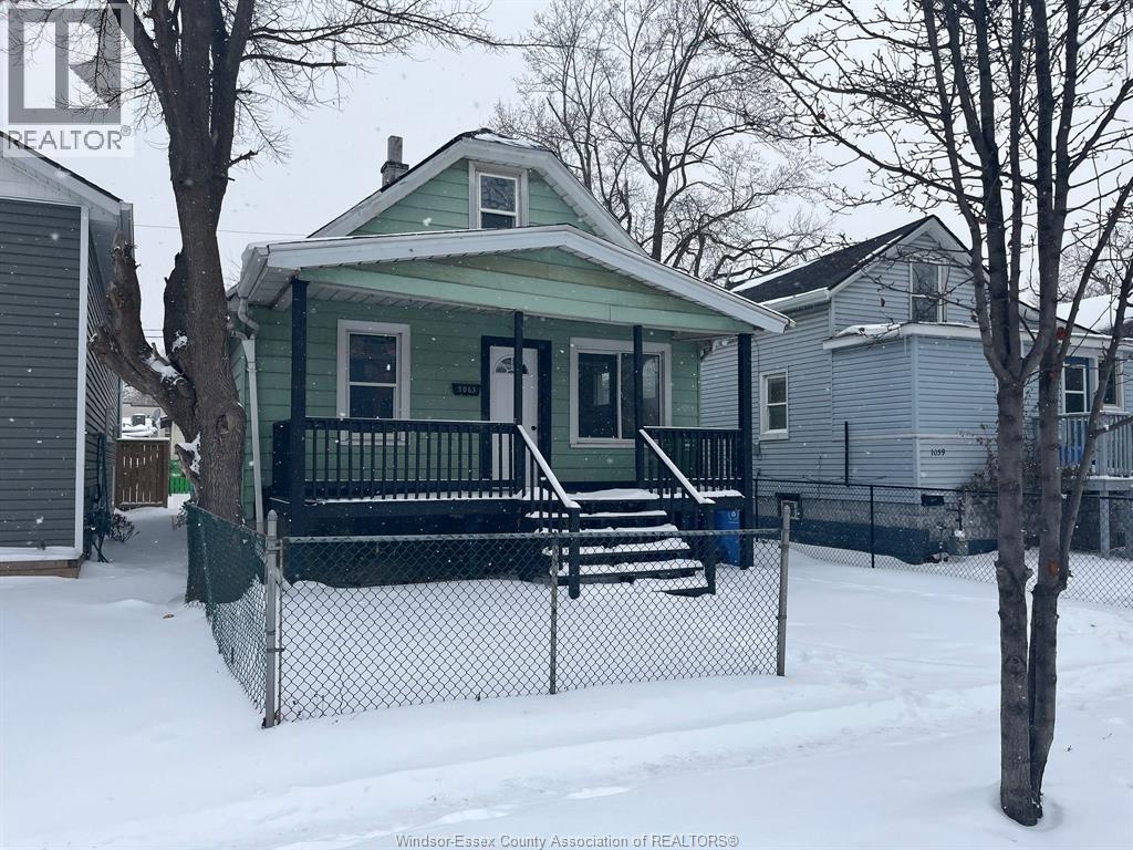 A green house with a black fence in the snow.