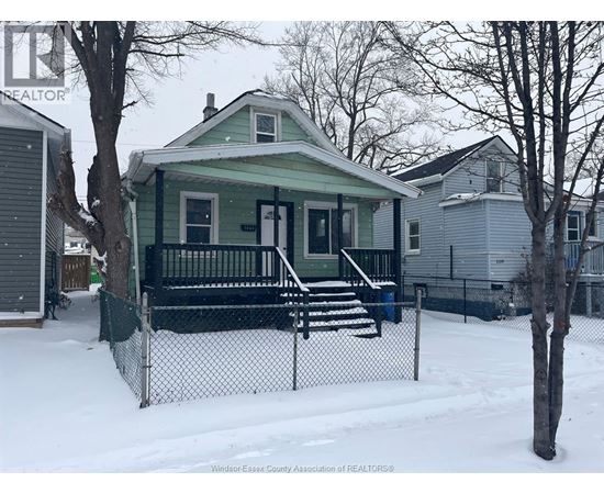 A green house with a black fence in the snow.