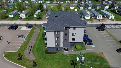 A large grey building with a black roof is surrounded by a parking lot.