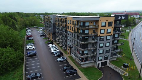 A parking lot with cars parked in front of a multi-story building with the number 2430 on it.