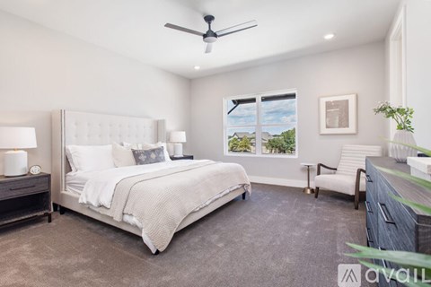 A bedroom with a large bed, a ceiling fan, and a window with a view of a house and trees.