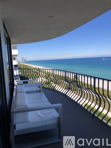 A balcony with a metal railing and a white chair overlooks a beach.