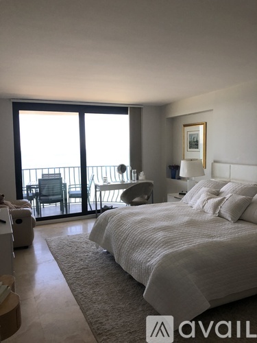A bedroom with a large bed and a balcony with chairs.