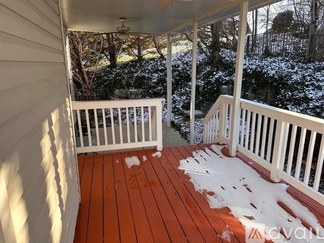 A deck with snow on the ground and trees in the background.