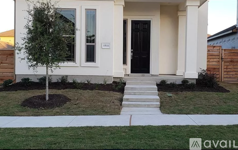 A white house with a black door and a tree in front.