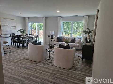 A living room with a large window, a dining table with chairs, and a couch with a white ottoman.