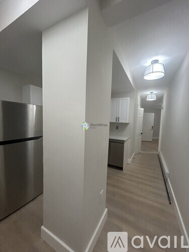 A long hallway with a stainless steel refrigerator on the left and a sign that says "Available" on the floor.