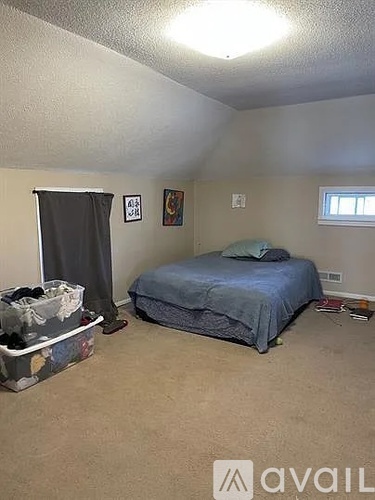 A bedroom with a bed, a window, and a trash bin.