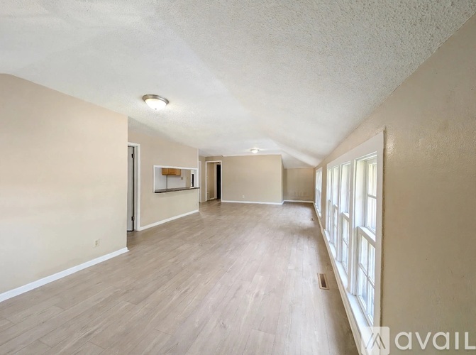 A spacious room with wooden flooring and a window on the right side.
