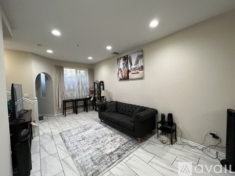 A living room with a black couch and a rug.