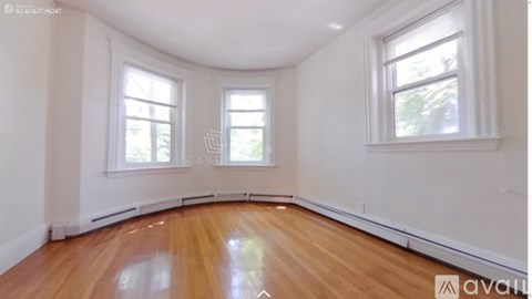 A room with wooden floors and white walls has two windows.