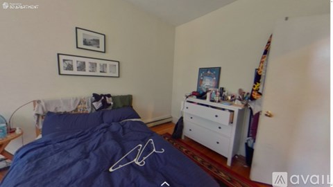 A bedroom with a blue bedspread and a white dresser with various items on top.