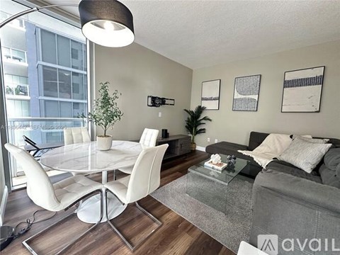 A modern living room with a grey couch, white chairs, and a glass table.