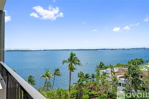 A balcony overlooks a body of water with palm trees in the foreground.