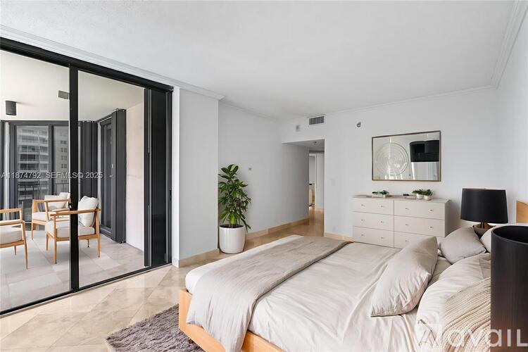 A bedroom with a large bed, a dresser, and a balcony with chairs.