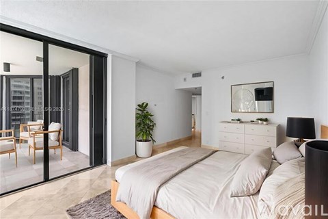 A bedroom with a large bed, a dresser, and a balcony with chairs.