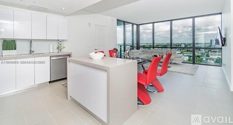A modern kitchen with white cabinets and a large island with red chairs.