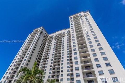 A tall white building with balconies and windows under a blue sky.