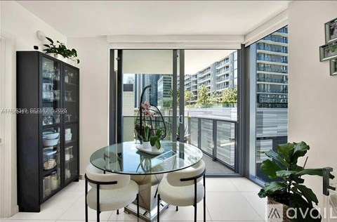 A modern dining room with a glass table and chairs, a black cabinet, and a view of the city outside the window.
