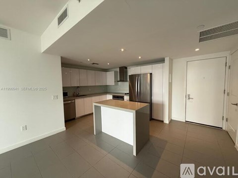 A modern kitchen with a central island and a refrigerator.