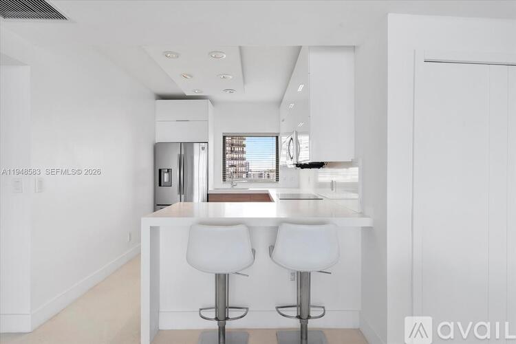 A modern kitchen with white cabinets and a bar area with two stools.